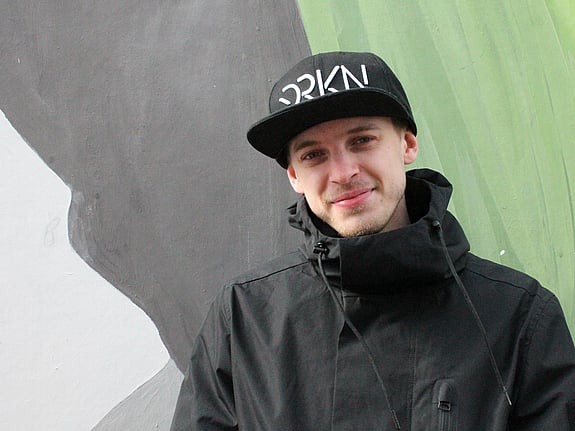 Kille i svart keps och jacka framför en ljusgrön fond